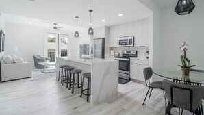 Een moderne keuken met een centraal eiland, barkrukken en een eethoek met een glazen tafel en stoelen.
