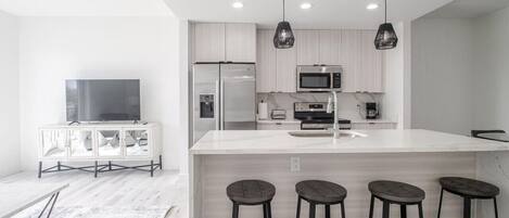 Una cocina moderna con una isla grande, taburetes de bar e iluminación colgante.