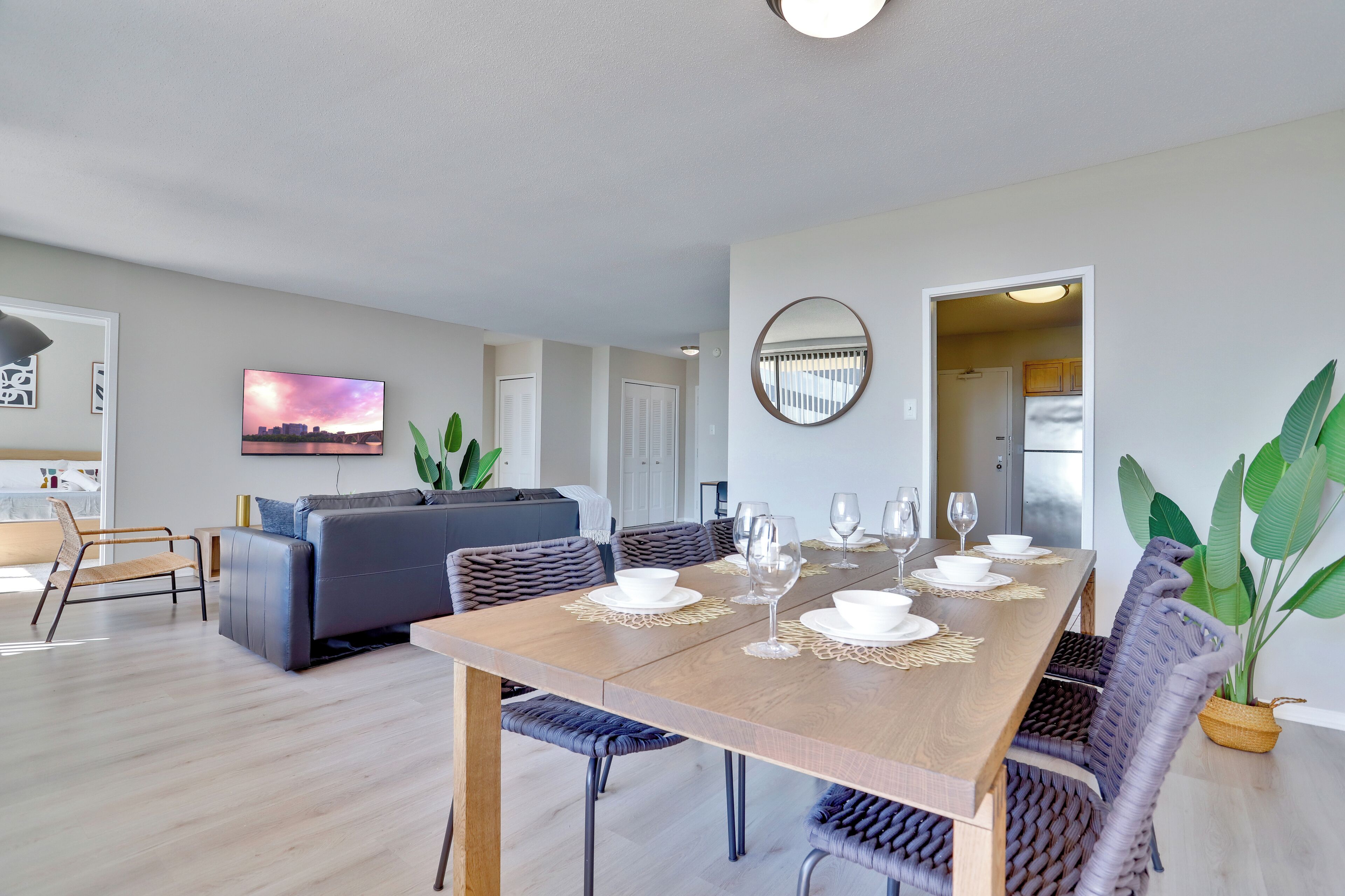 A modern living room with a dining area, a gray sofa, a large mirror, and a view of the city.