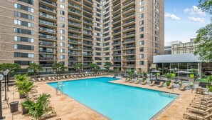 A swimming pool surrounded by lounge chairs and a tall building in the background. - Comfort Living Alexandria Apts (Arlington)
