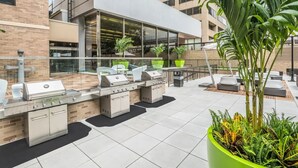 An outdoor patio with a barbecue area, seating, and potted plants. - Comfort Living Alexandria Apts (Arlington)