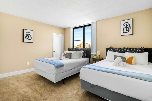 A hotel room with two beds, a window with a city view, and artwork on the walls.