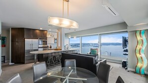 A modern kitchen with dark wood cabinets, stainless steel appliances, and a large window overlooking a body of water. - NewMark Towers Water Wheel Sea Views (Seattle)