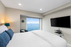 A bedroom with a large bed, a TV mounted on the wall, and a window with a view of the sea. - NewMark Towers Water Wheel Sea Views (Seattle)