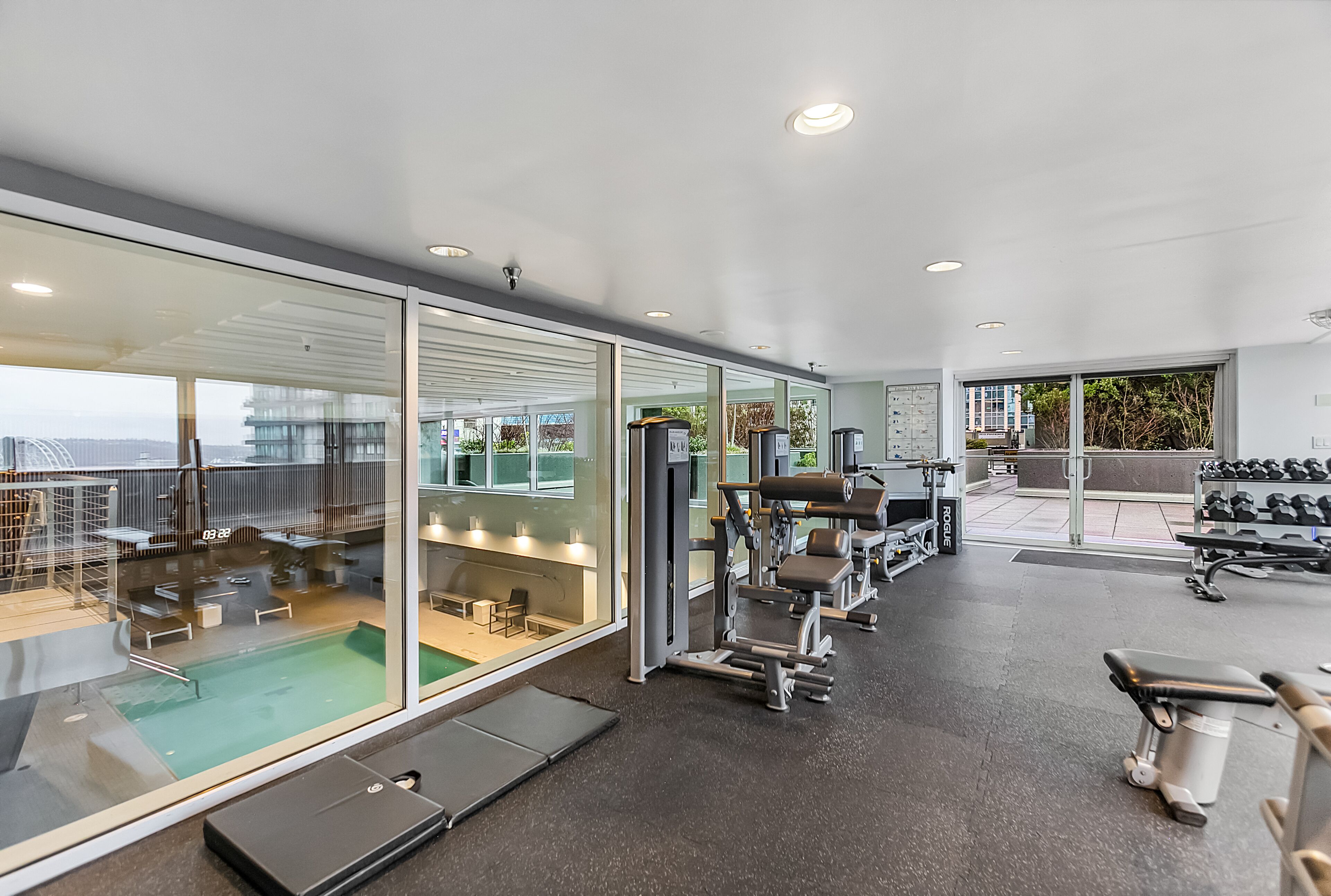 Un gimnasio moderno con paredes de vidrio, diversos equipos de ejercicio y una zona de piscina.