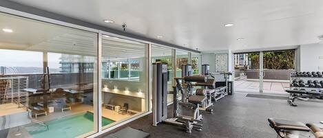 Un gimnasio moderno con paredes de vidrio, diversos equipos de ejercicio y una zona de piscina.