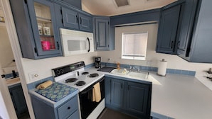 A compact kitchen with blue cabinets, a white stove, a microwave, and a sink.