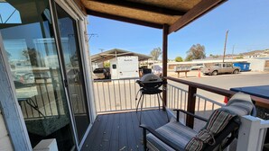 A covered deck with a sliding glass door, a barbecue grill, and a striped cushion on a bench.