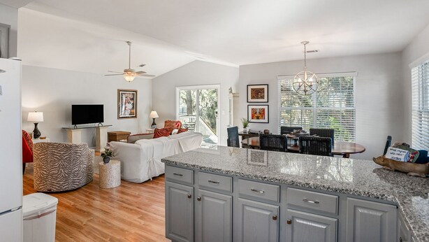 A spacious kitchen with granite countertops, a dining area with wicker chairs, and a living room with a sofa and television. - Tidal Wave Retreat (Beaufort)