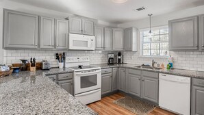 A kitchen with grey cabinets, a white microwave, a stove, and a dishwasher. - Tidal Wave Retreat (Beaufort)