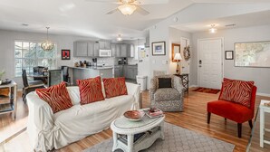 A modern living room with a sofa, armchairs, and a coffee table. There is a kitchen in the background with cabinets and a microwave. - Tidal Wave Retreat (Beaufort)