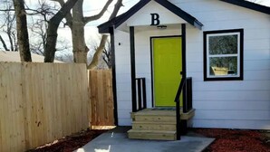 A small white building with a bright green door, a wooden fence, and a concrete path leading to it.