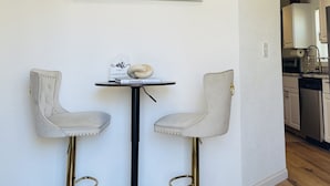 A dining area with two white bar stools, a round table, and a chandelier.