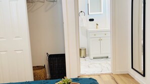 A bedroom with a bed, a bedside table with a plant, a mirror, and a wardrobe.
