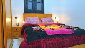 A bed with a colorful bedspread and two pillows, a wooden headboard, and two bedside lamps.