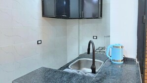 A kitchen with a granite countertop, a stainless steel sink, a blue kettle, and a black cabinet above the sink.