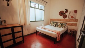 Een kleine, compacte kamer met een bed, een tafeltje en een raam.
