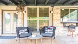 An outdoor patio with two black wicker chairs, a small round table, and a fan. - Fireplace, Fire Pit, Turf Backyard | Central ATX (Austin)