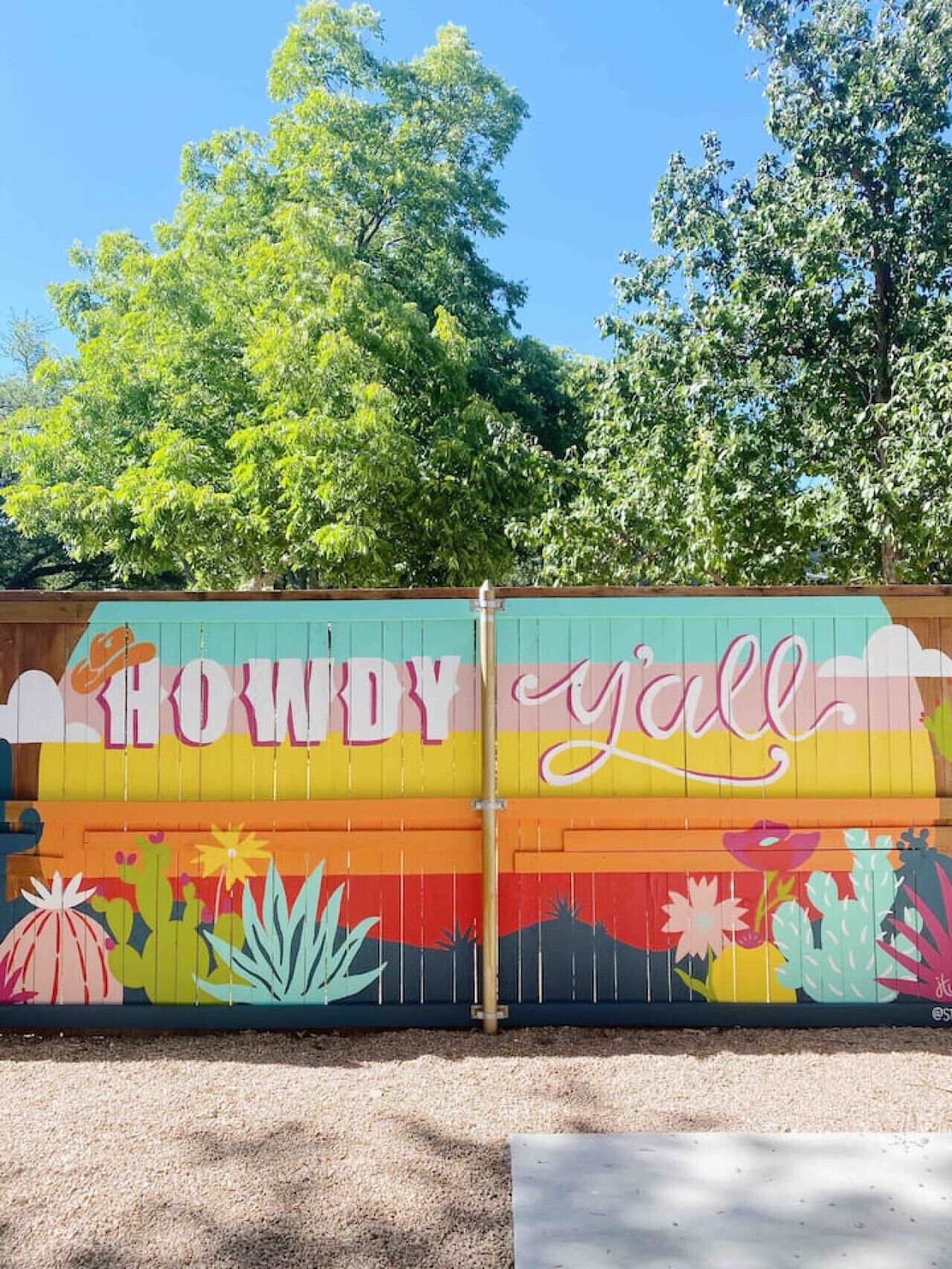 A colorful mural on a fence with the words "HOWDY y'all" and various plants.