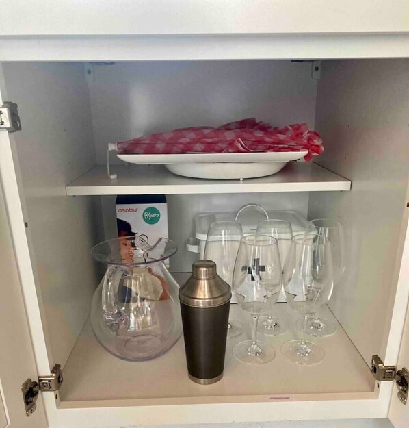A cabinet with a white interior, containing a white plate with a red cloth, a box labeled 'asobo Hydro', and several clear glasses and a cocktail shaker. - Historic Area | Walk 2 Southwestern Campus! (Georgetown)