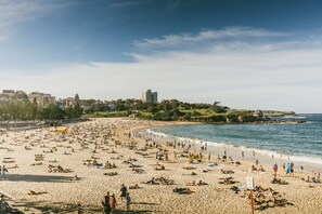 A crowded beach with people sunbathing and swimming, a clear sky, and buildings in the background. - Coogee Beach Penthouse apartment (Coogee)