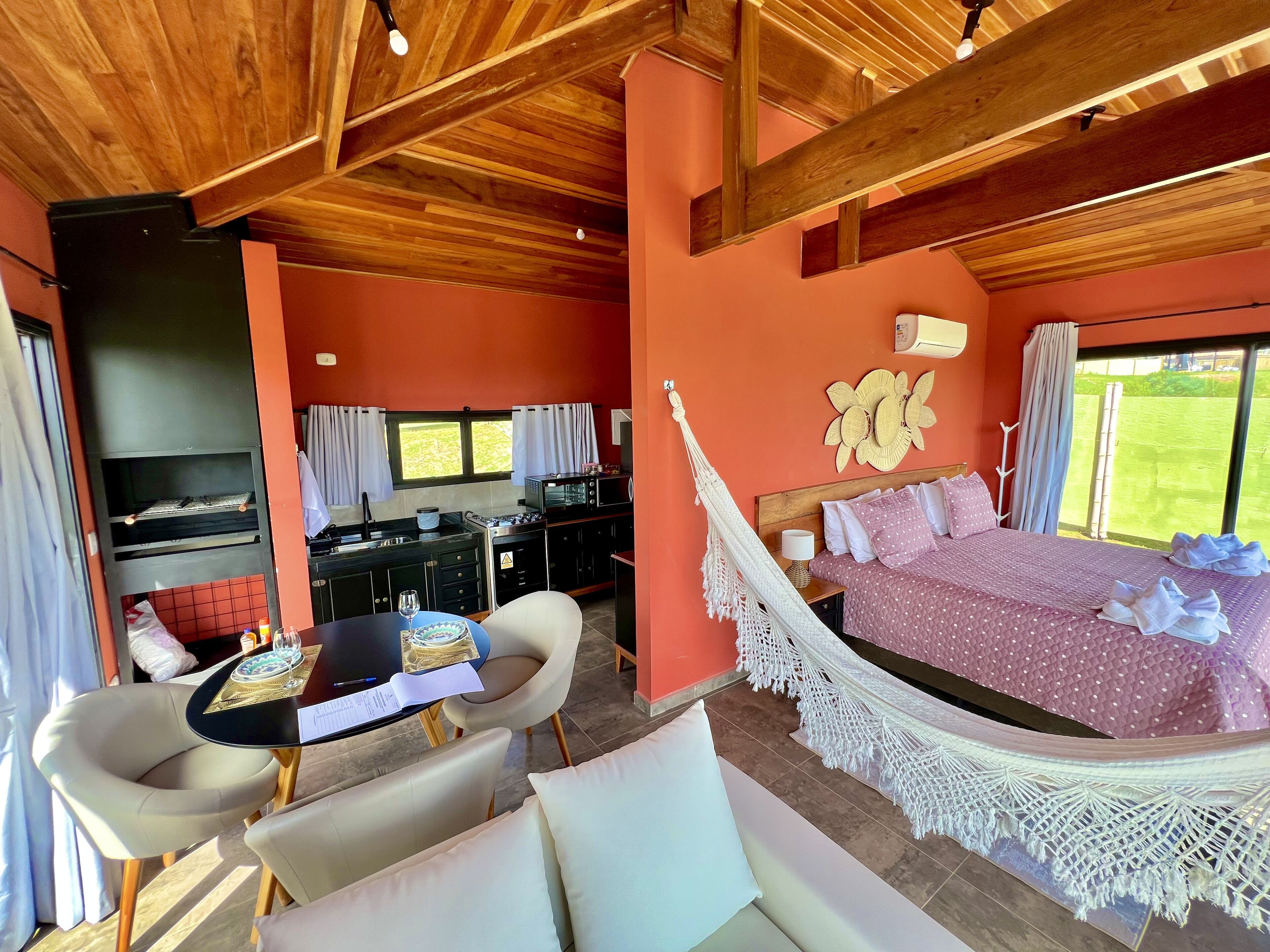 A cozy room with a bed, a dining table, chairs, a kitchen area, and a hammock.