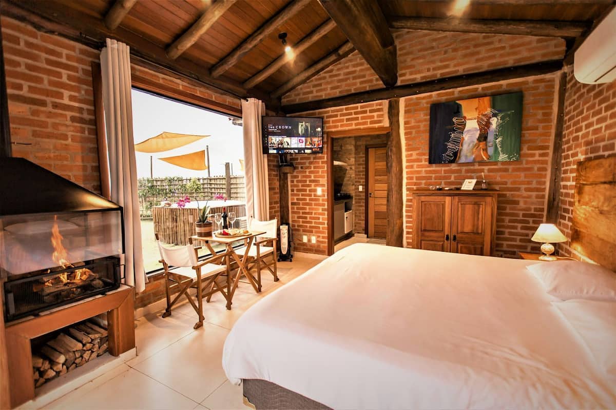 A hotel room with a fireplace, a bed, a TV, and a balcony with outdoor seating.