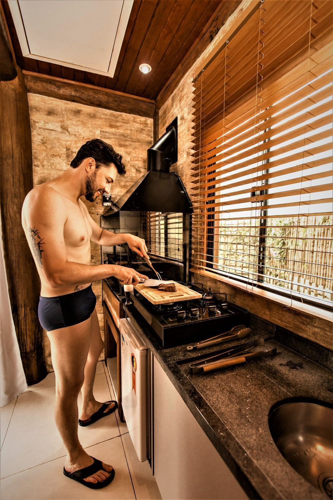 A person cooking in a modern kitchen with wooden accents and a large window.