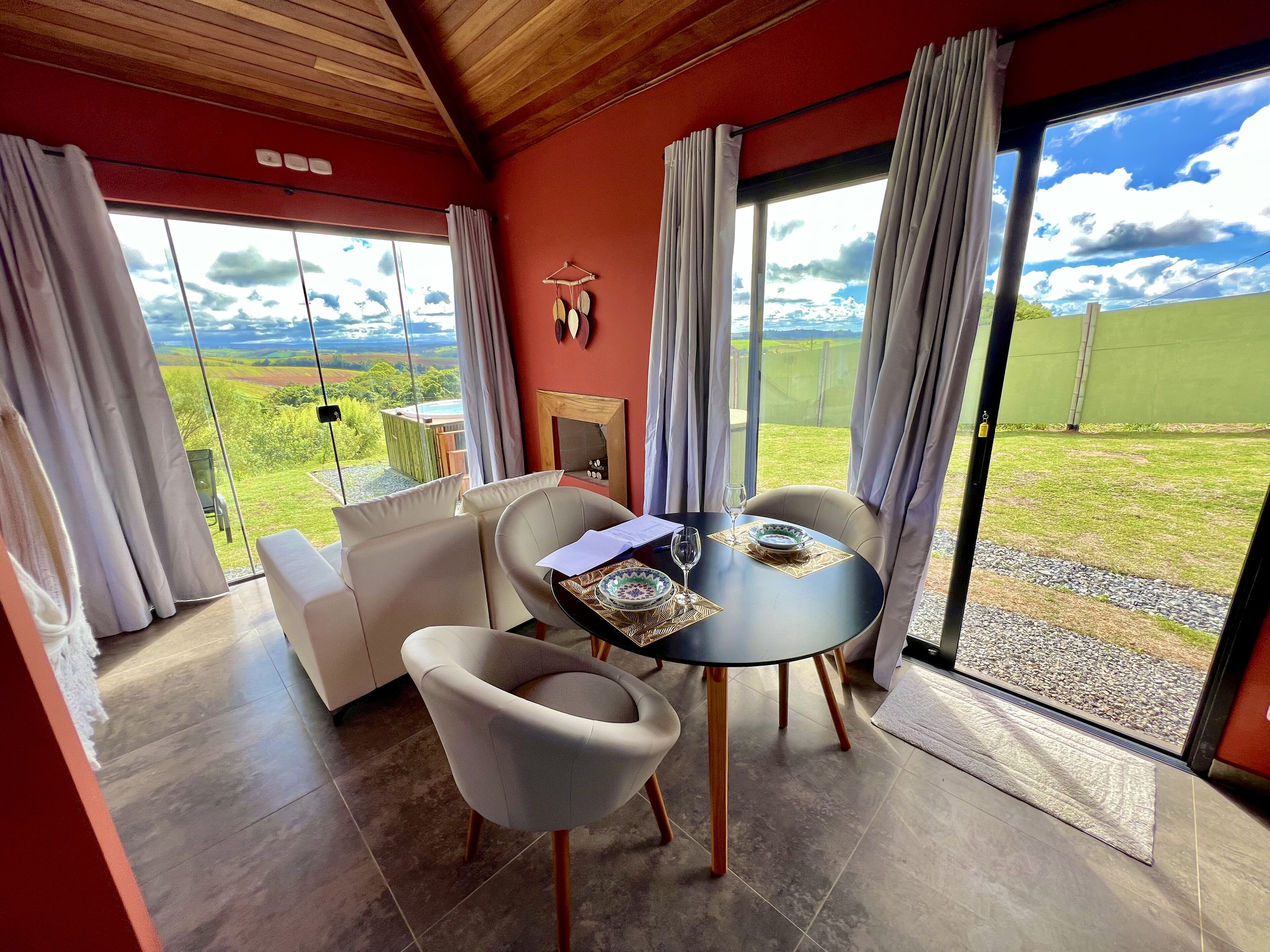 Ein Essbereich mit einem Tisch für zwei Personen, einer Couch und Blick auf eine grüne Landschaft durch große Fenster.