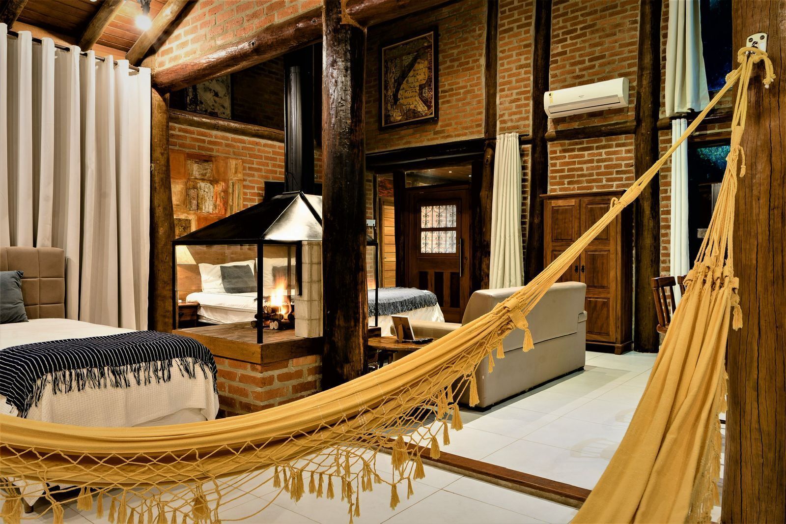A rustic room with a hammock, a fireplace, a bed, and a wooden ceiling.