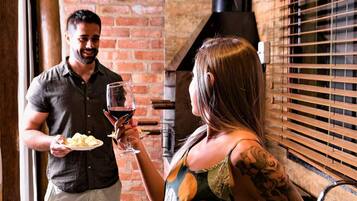A man and a woman in a rustic kitchen with brick walls, a wooden ceiling, and a black stove.