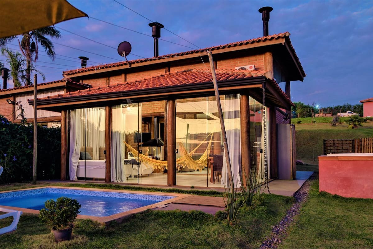 A modern house with a glass-enclosed patio, a swimming pool, and a hammock.