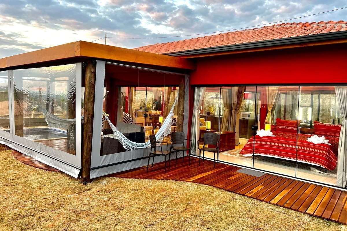 A modern house with a glass-enclosed patio, a hammock, and a red-roofed bedroom.