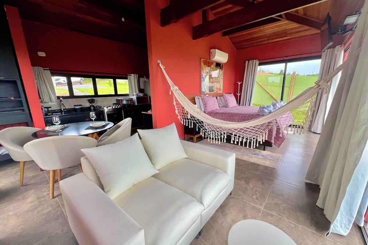 A modern living room with a white sofa, a hammock, and a dining area with a table and chairs.