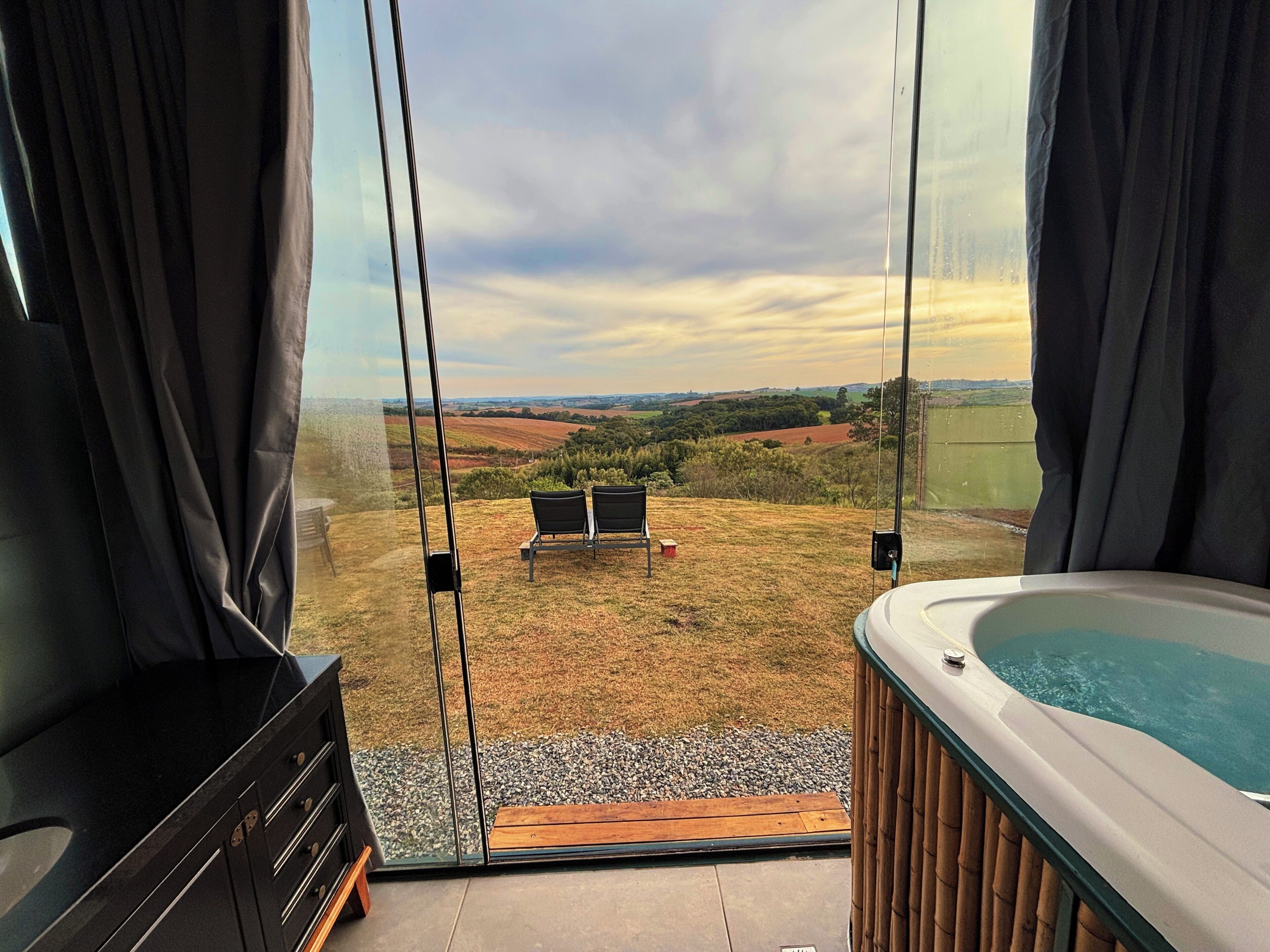 A room with a large window offering a view of a grassy area with chairs and a hot tub.