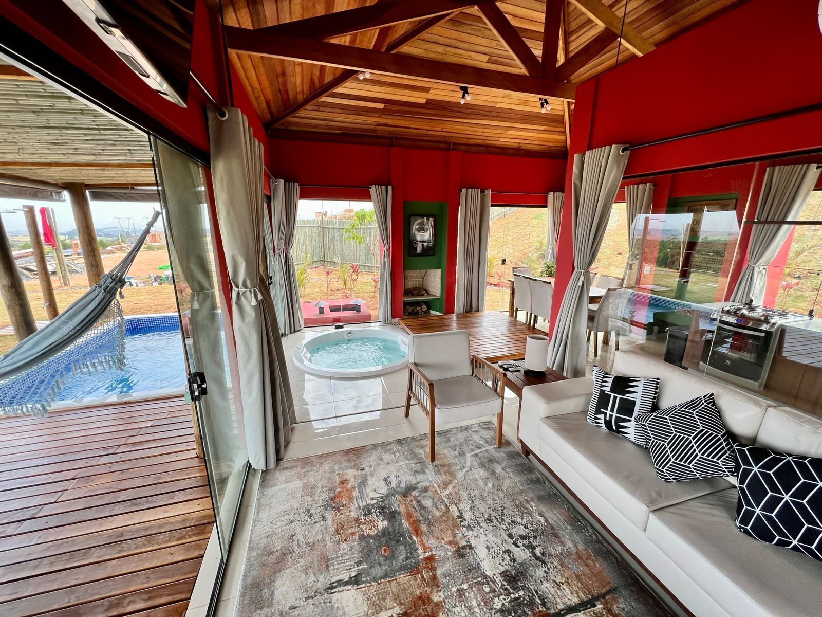 Un espacio interior acogedor con techo de madera, un jacuzzi, zona de comedor y vistas a una piscina y área exterior.