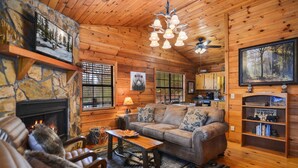 Ein gemütliches Blockhaus-Interieur mit Kamin aus Naturstein, Holzwänden, einer bequemen Couch und einem Essbereich.