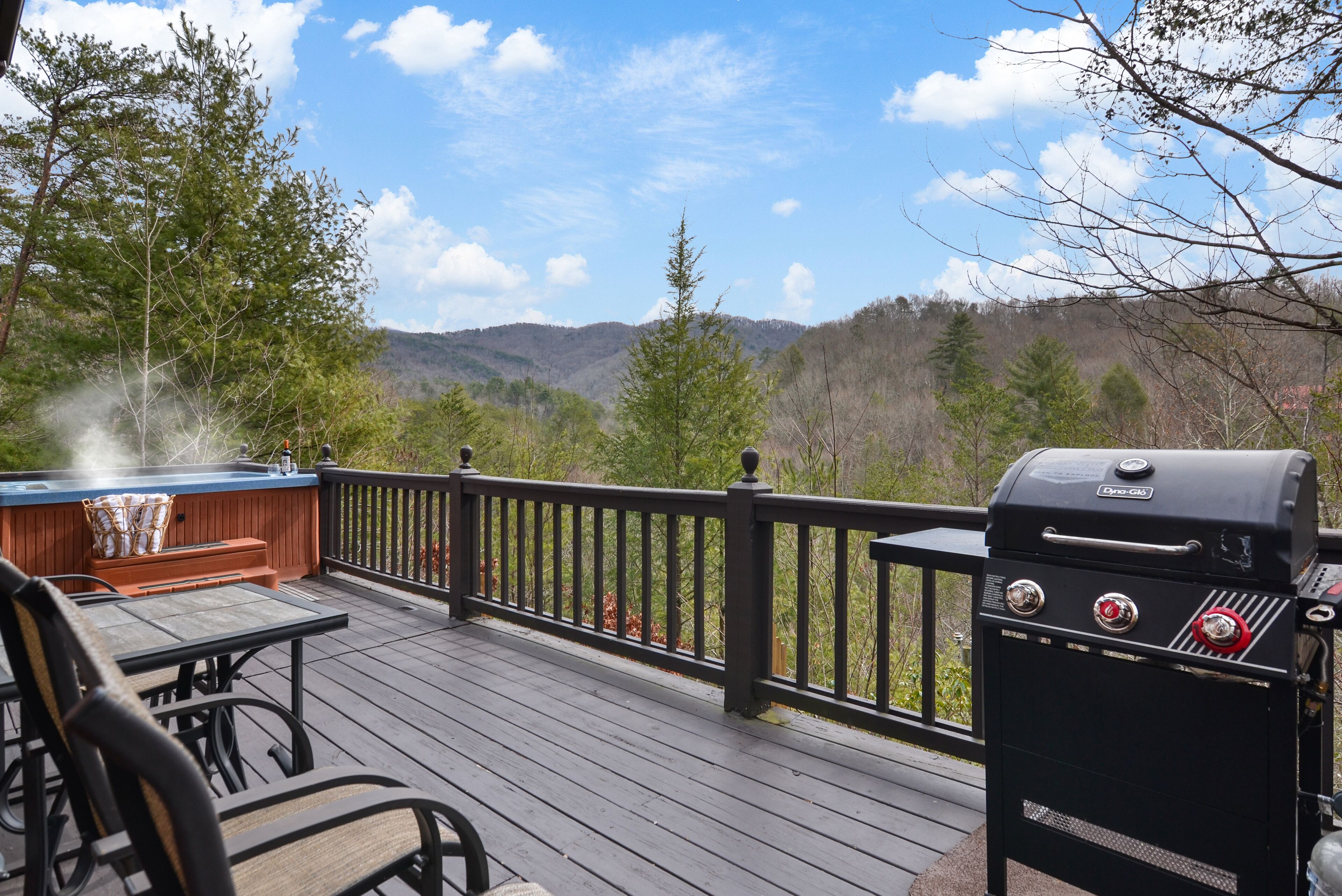 A deck with a grill and hot tub, overlooking a forested mountain area.