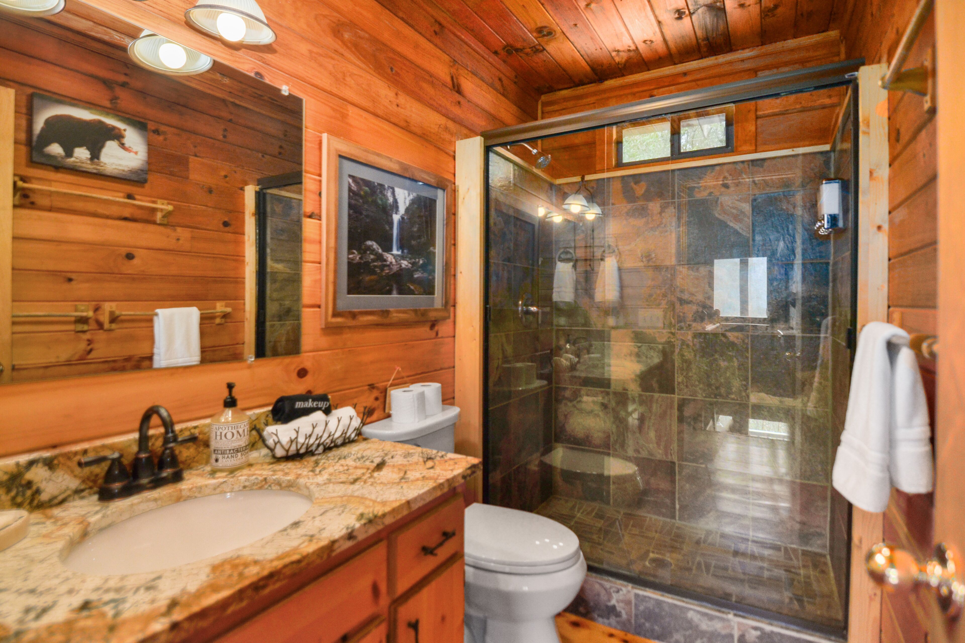 A wooden cabin bathroom with a sink, toilet, and glass-enclosed shower.