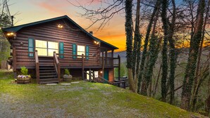 Eine Blockhütte mit Veranda, Treppe und Blick auf den umliegenden Wald.