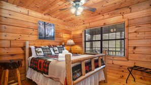Ein Schlafzimmer einer Holzhütte mit Bett, Deckenventilator, Fenster mit Jalousien und Wandbild.