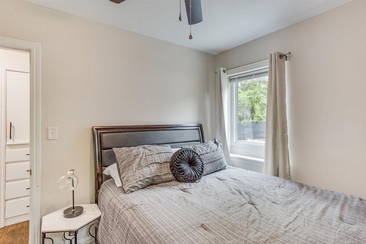 Un dormitorio con cama, mesita de noche, lámpara y ventana con cortinas.
