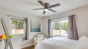 A bedroom with a bed, a ceiling fan, two windows with curtains, a chair, and a painting on the wall. - Nearby Wesley. Pickle Ball + Family Fun! (Wichita)