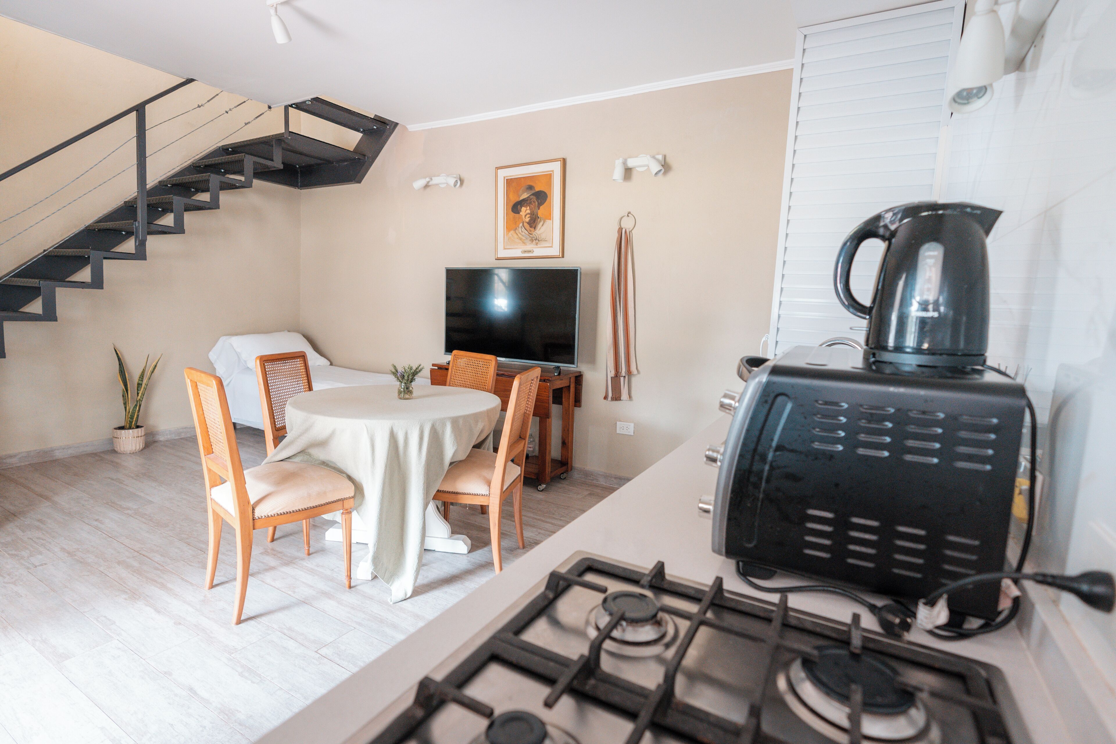 Una cocina moderna con estufa a gas, comedor con mesa redonda y sillas, televisor de pantalla plana y una escalera.