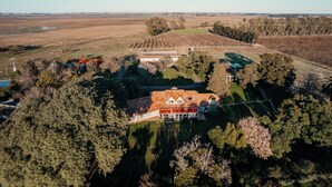 Vista aérea de una gran propiedad con amplios campos, una casa principal de techo rojo y árboles circundantes.