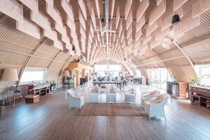 A spacious interior with high ceilings, wooden flooring, and a central seating area with white wicker furniture. - La Santina Posada & Experiencia de Campo (Río Tala)