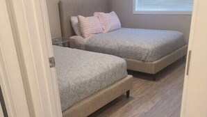 A bedroom with two beds, a window with blinds, and a door.