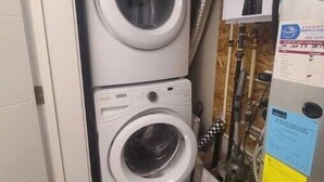 A compact laundry room with two stacked washing machines, a water heater, and visible plumbing.