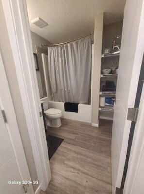 A modern bathroom with a toilet, shower, and storage shelves. - Luxury Condo For Rent
 (Calgary)