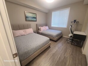 A bedroom with two beds, a desk, and a window. - Luxury Condo For Rent
 (Calgary)